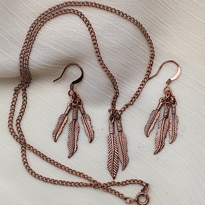 Complete feather jewelry set with copper tone necklace and dangle earrings arranged in styled flat lay, western boho jewelry with nature inspired feather design, statement necklace paired with lightweight earrings, gift for her perfect for country western outfits, festival looks and vintage style costume jewelry