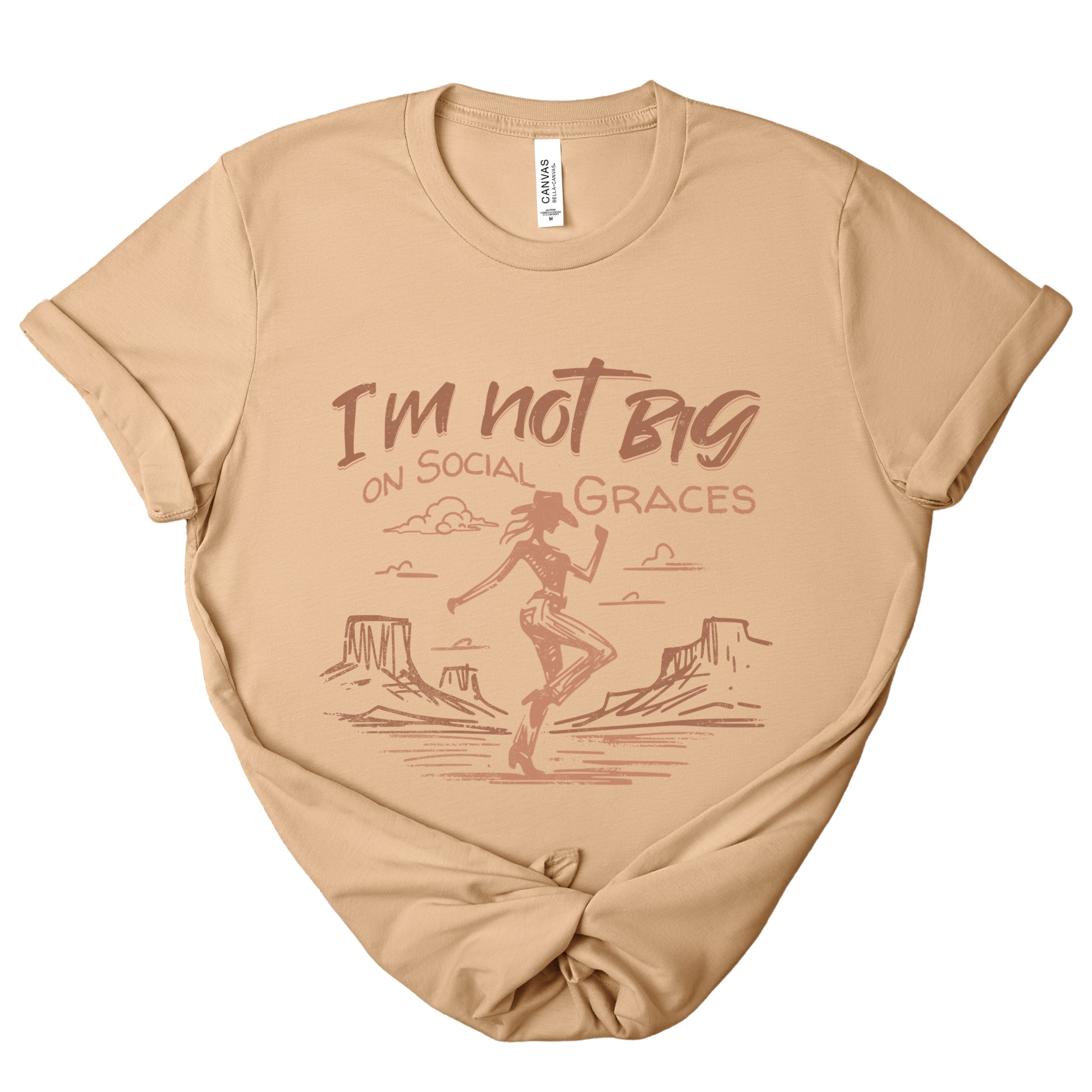 Western graphic tee in sand dune color featuring a vintage cowgirl design with “I’m not big on social graces” text, soft neutral boutique t-shirt styled in a relaxed unisex fit