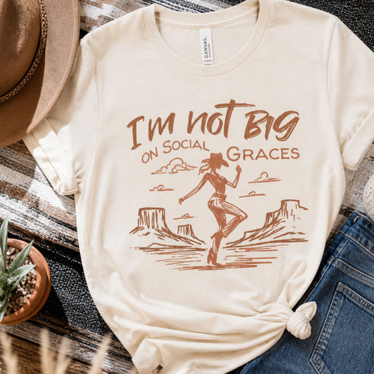 Western graphic tee in natural color styled in a flat lay with denim shorts and cowboy hat, featuring a vintage cowgirl design and neutral boutique outfit aesthetic