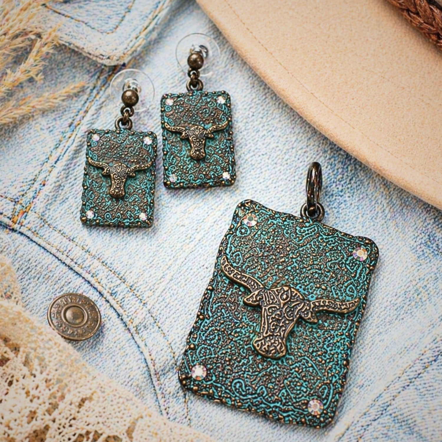 Western longhorn pendant and matching earrings set displayed on light denim flatlay with rustic textures, featuring turquoise patina metal, engraved concho details, and rhinestone accents, Southwestern cowgirl jewelry set styled with neutral tones, perfect for Western fashion outfits, rodeo wear, country concerts, and rustic boho accessories