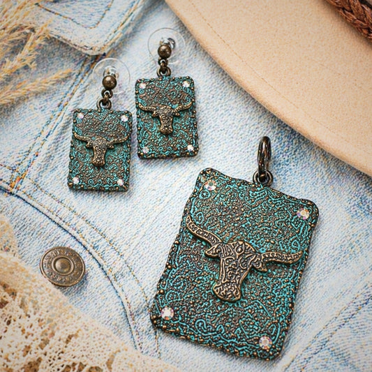Western longhorn pendant and matching earrings set displayed on light denim flatlay with rustic textures, featuring turquoise patina metal, engraved concho details, and rhinestone accents, Southwestern cowgirl jewelry set styled with neutral tones, perfect for Western fashion outfits, rodeo wear, country concerts, and rustic boho accessories