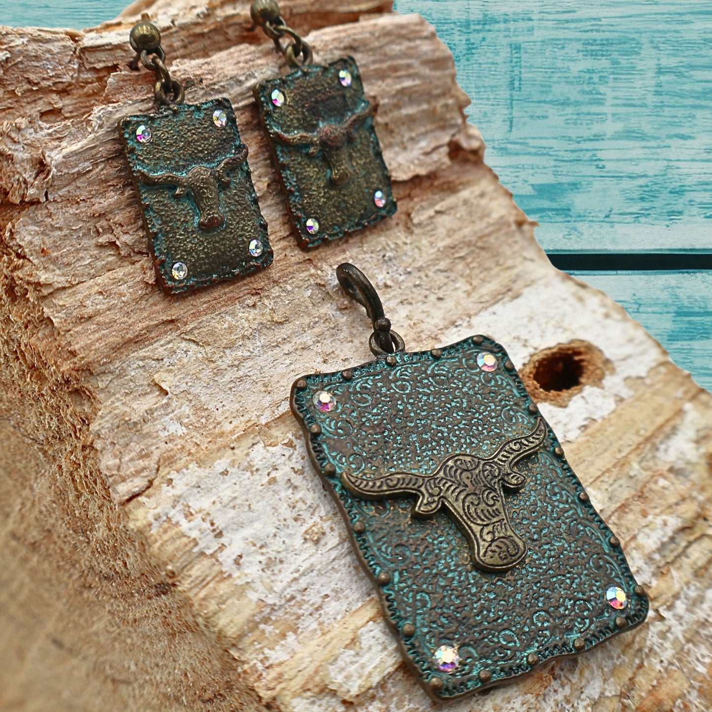 Western longhorn jewelry set featuring turquoise patina pendant and matching dangle earrings displayed on rustic wood with turquoise painted background, ornate concho detailing with rhinestone accents adds Southwestern cowgirl charm, Western style accessory perfect for rodeo outfits, country concerts, boho fashion, and rustic Western home and fashion styling