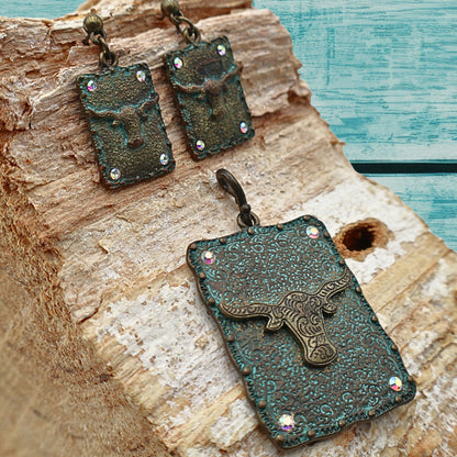 Western longhorn jewelry set featuring turquoise patina pendant and matching dangle earrings displayed on rustic wood with turquoise painted background, ornate concho detailing with rhinestone accents adds Southwestern cowgirl charm, Western style accessory perfect for rodeo outfits, country concerts, boho fashion, and rustic Western home and fashion styling