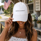 Woman wearing cream western ponytail trucker hat with small town sweetheart embroidery and cow print longhorn undervisor in rustic country setting