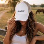 Woman wearing cream western trucker hat with save a horse embroidery outdoors in a country-inspired western setting