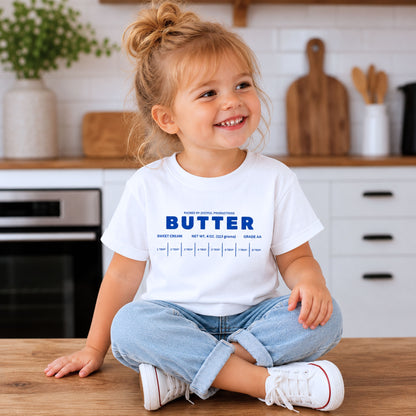 Toddler girl wearing white butter birthday shirt with retro foodie graphic and sweet cream bakery aesthetic. Boutique preschool outfit styled for birthday celebrations, baking themes, and trendy kids fashion photography.