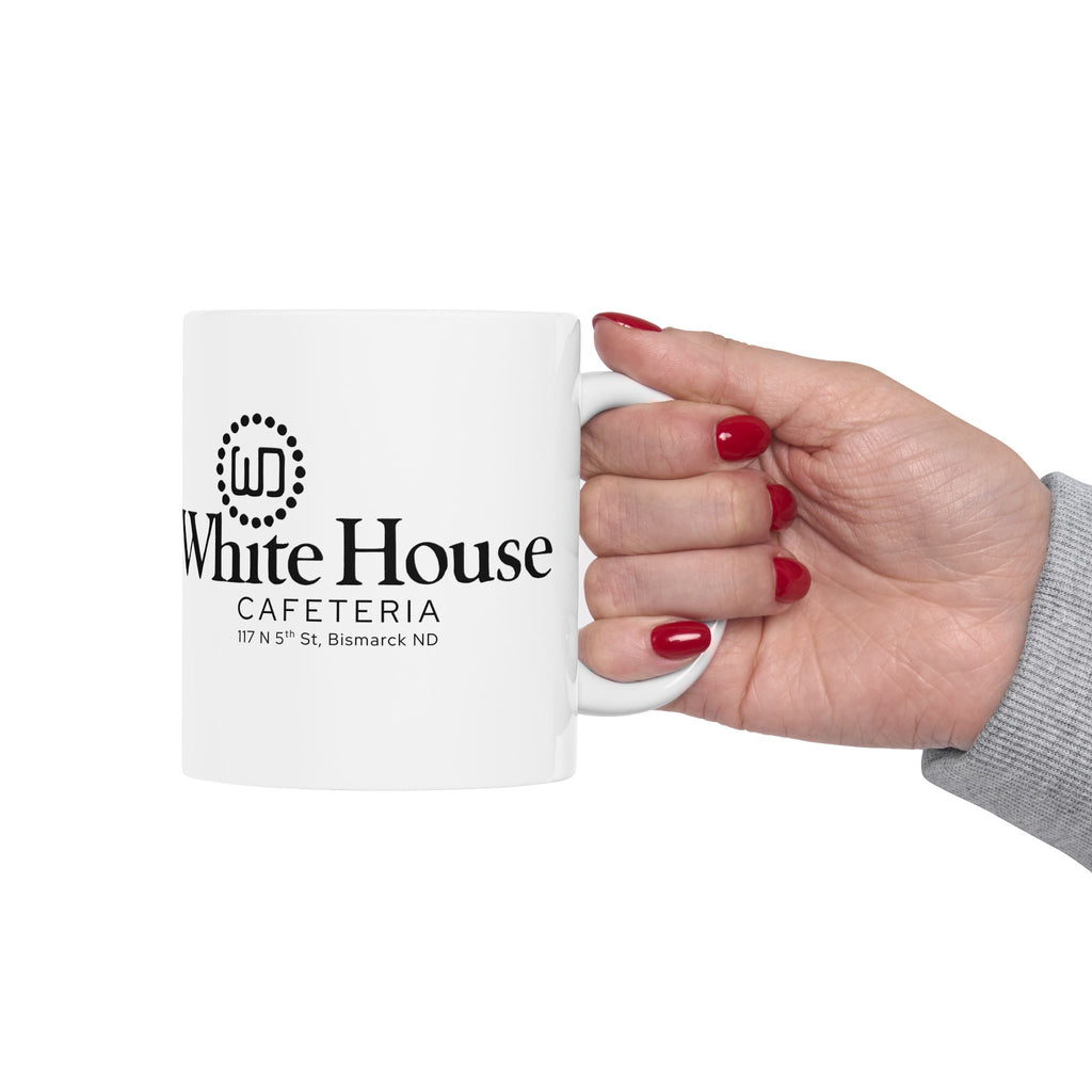 White 11-ounce ceramic coffee mug held by a hand with red nail polish against a white background. The visible side features the black White House Cafeteria logo and the original 117 North 5th Street address in Bismarck, North Dakota.