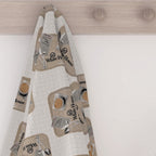 White House Cafeteria kitchen tea towel hanging from a light wood wall hook. The soft, light oatmeal towel displays a repeating pattern of vintage cafeteria trays with coffee, silverware, a handwritten Cheese Buttons and caramel roll order, and the White House logo.