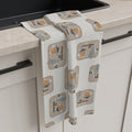 White House Cafeteria tea towel draped beside a black kitchen sink in a modern cream kitchen. The light oatmeal towel features a repeating pattern of vintage cafeteria trays with coffee, silverware, a guest check and the White House name from Bismarck, North Dakota.