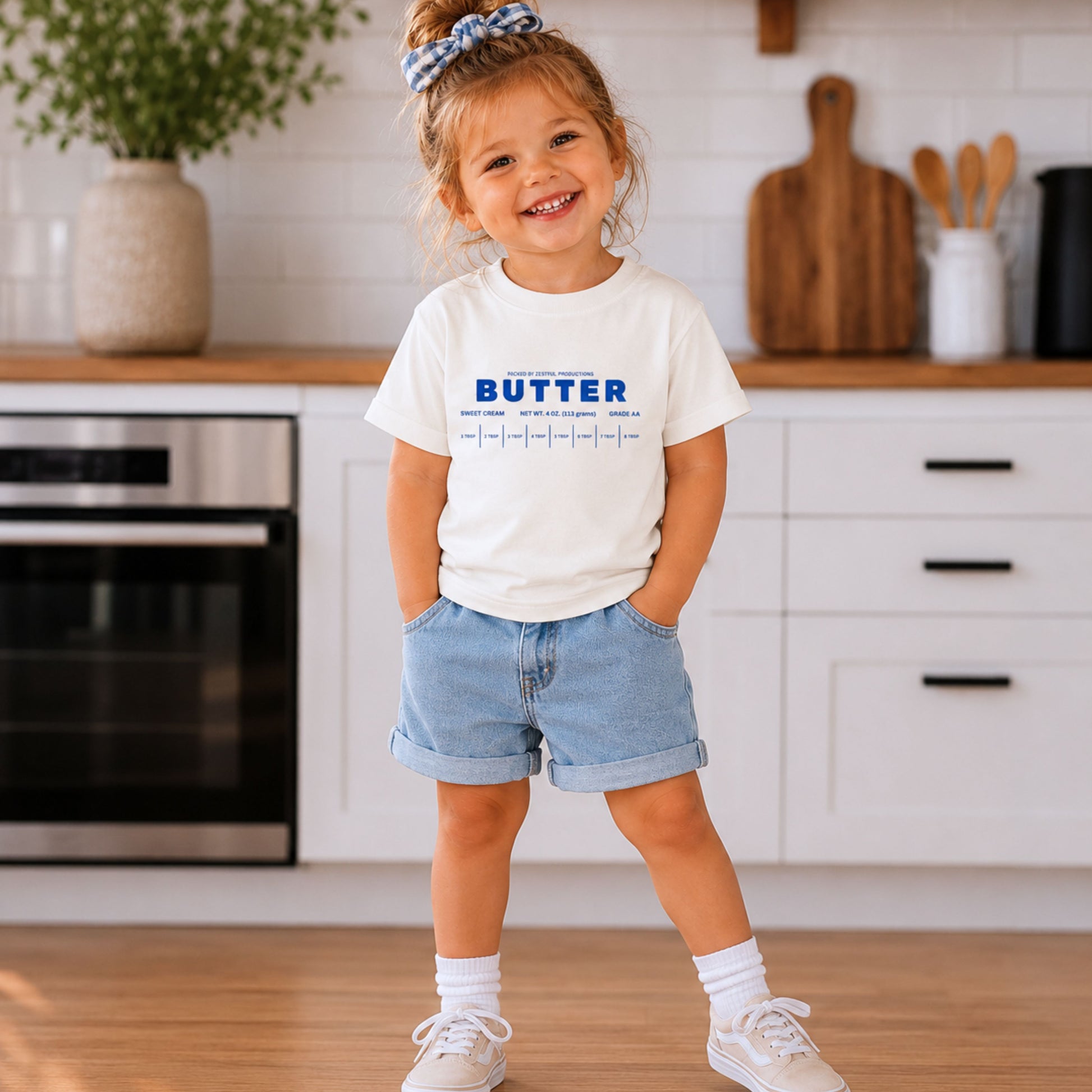 Toddler girl wearing white retro butter toddler shirt with foodie inspired bakery graphic. Boutique birthday outfit styled for preschool fashion, playful celebrations, family photos, and trendy everyday kidswear.