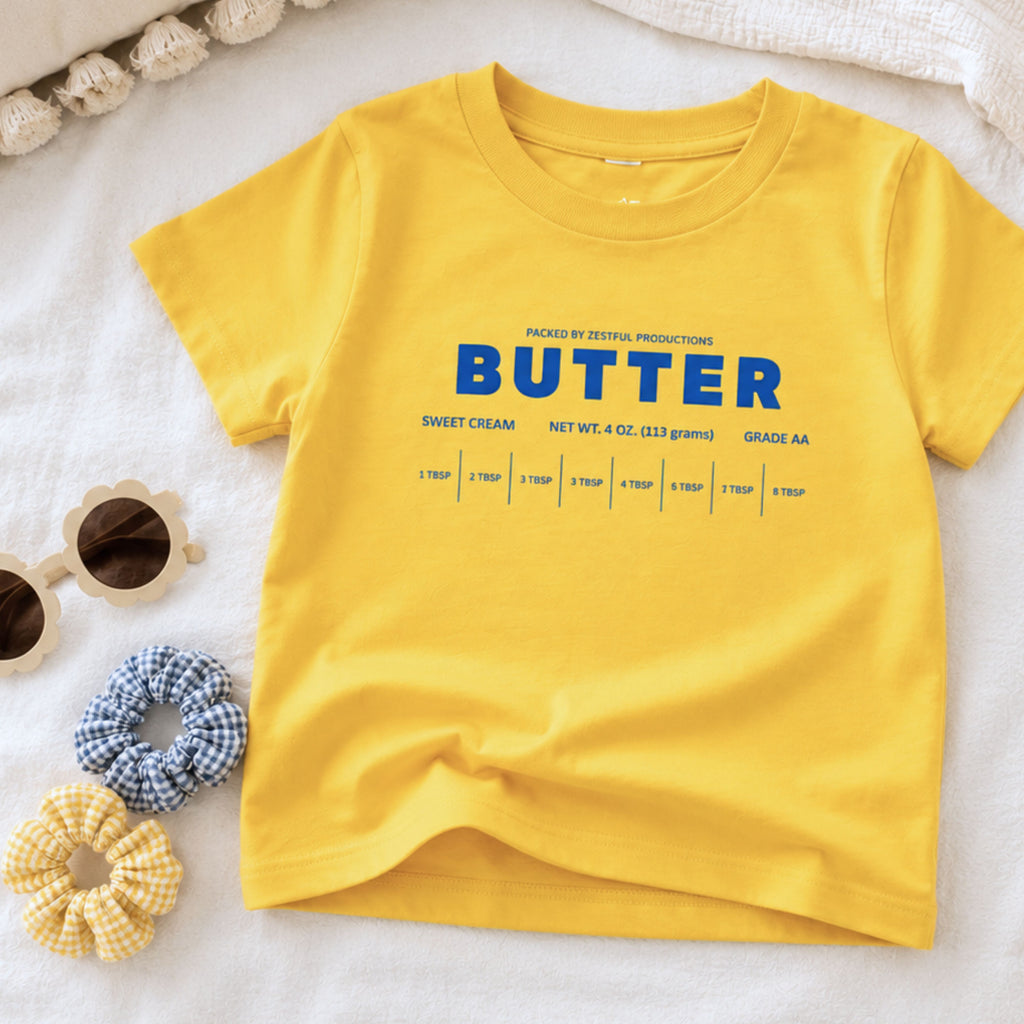 Yellow butter toddler tee flat lay with retro sweet cream baking design and foodie inspired packaging graphic. Boutique birthday shirt styled for preschool outfits, playful baking themes, and aesthetic kids apparel.
