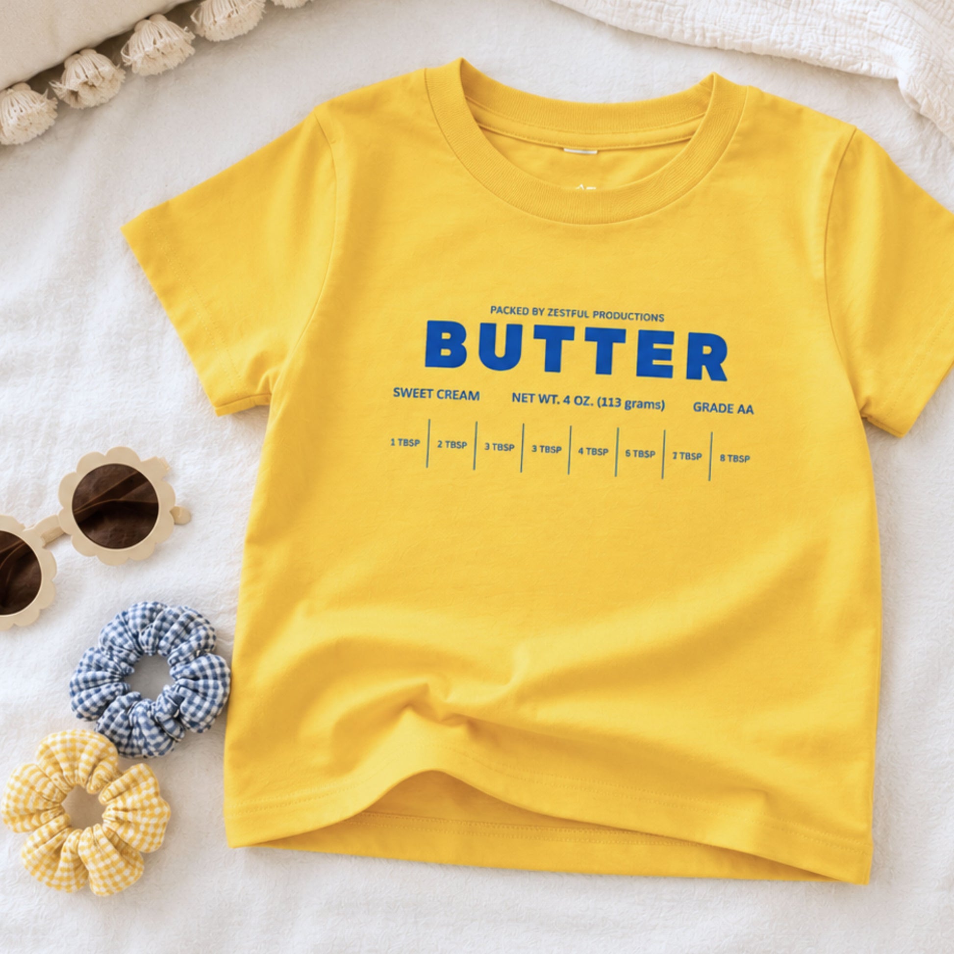 Yellow butter toddler tee flat lay with retro sweet cream baking design and foodie inspired packaging graphic. Boutique birthday shirt styled for preschool outfits, playful baking themes, and aesthetic kids apparel.