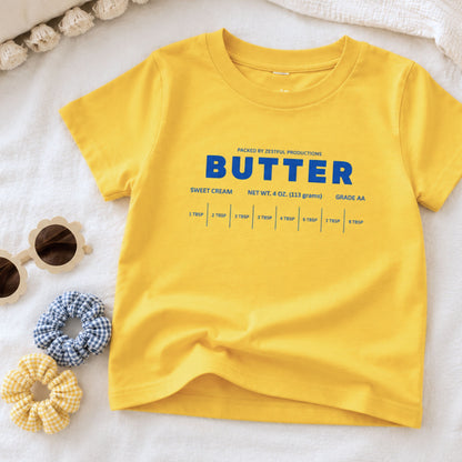 Yellow butter toddler tee flat lay with retro sweet cream baking design and foodie inspired packaging graphic. Boutique birthday shirt styled for preschool outfits, playful baking themes, and aesthetic kids apparel.