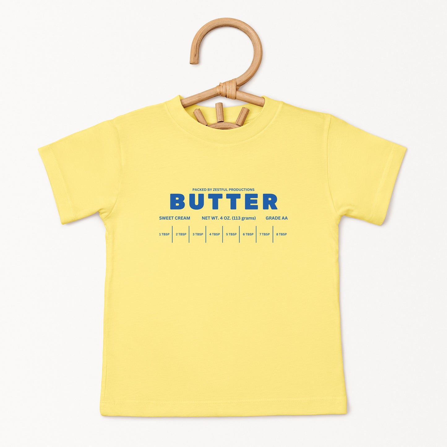 Yellow butter toddler tee displayed on wooden hanger featuring retro sweet cream baking graphic and foodie inspired design. Boutique kids birthday shirt perfect for preschool outfits, parties, and playful everyday wear.