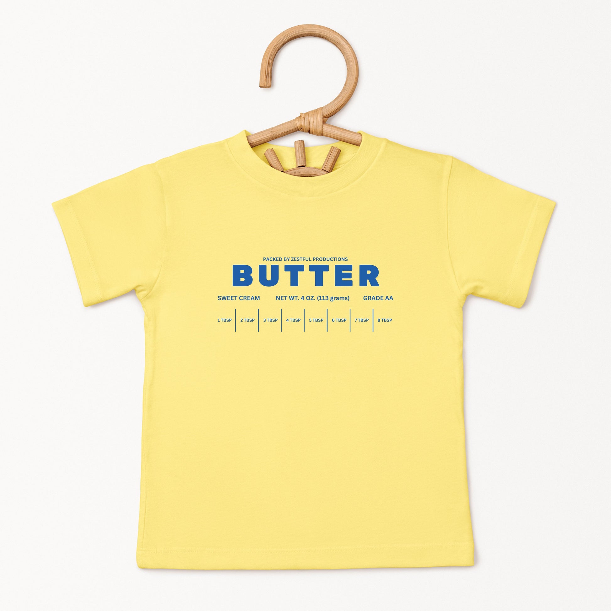 Yellow butter toddler tee displayed on wooden hanger featuring retro sweet cream baking graphic and foodie inspired design. Boutique kids birthday shirt perfect for preschool outfits, parties, and playful everyday wear.