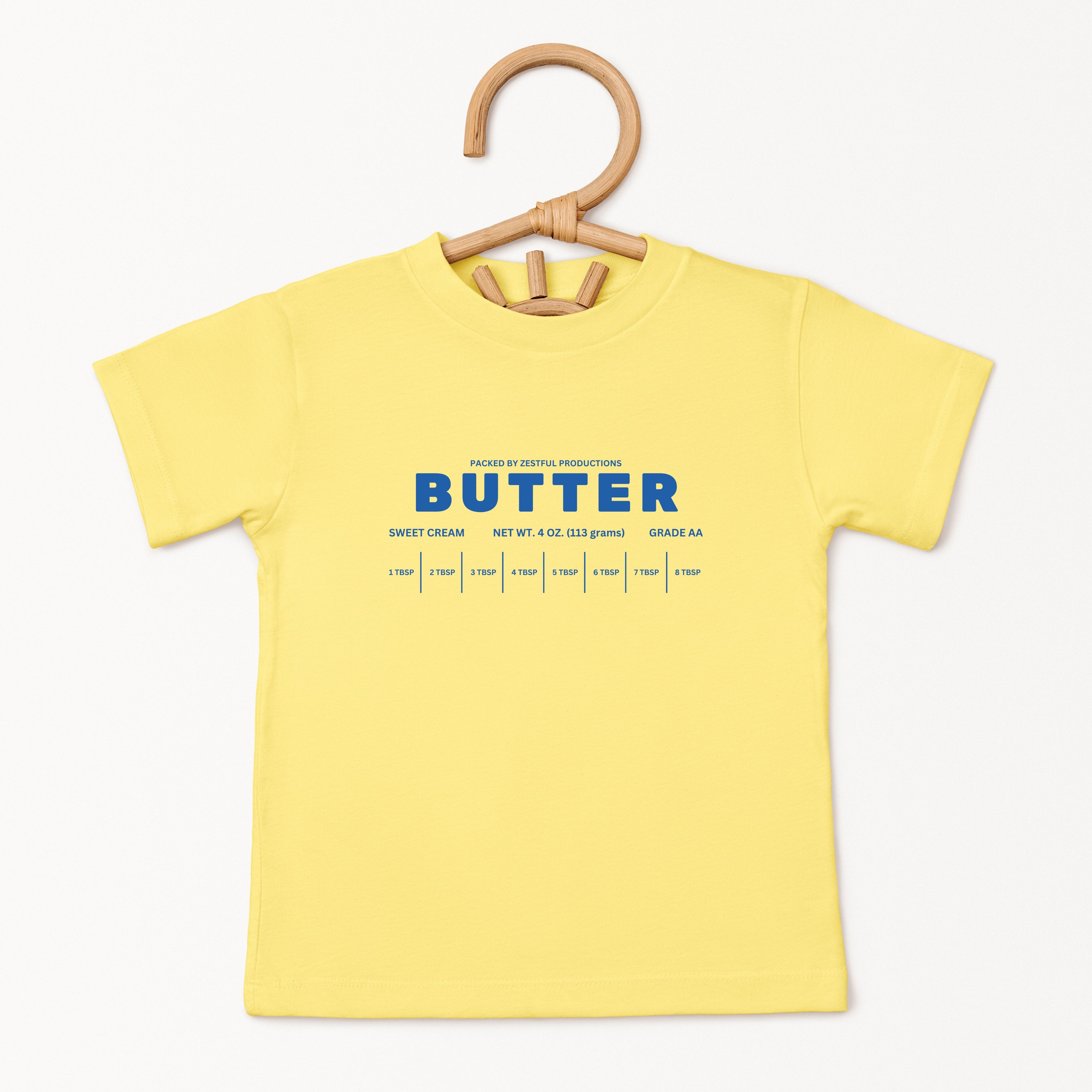 Yellow butter toddler tee displayed on wooden hanger featuring retro sweet cream baking graphic and foodie inspired design. Boutique kids birthday shirt perfect for preschool outfits, parties, and playful everyday wear.