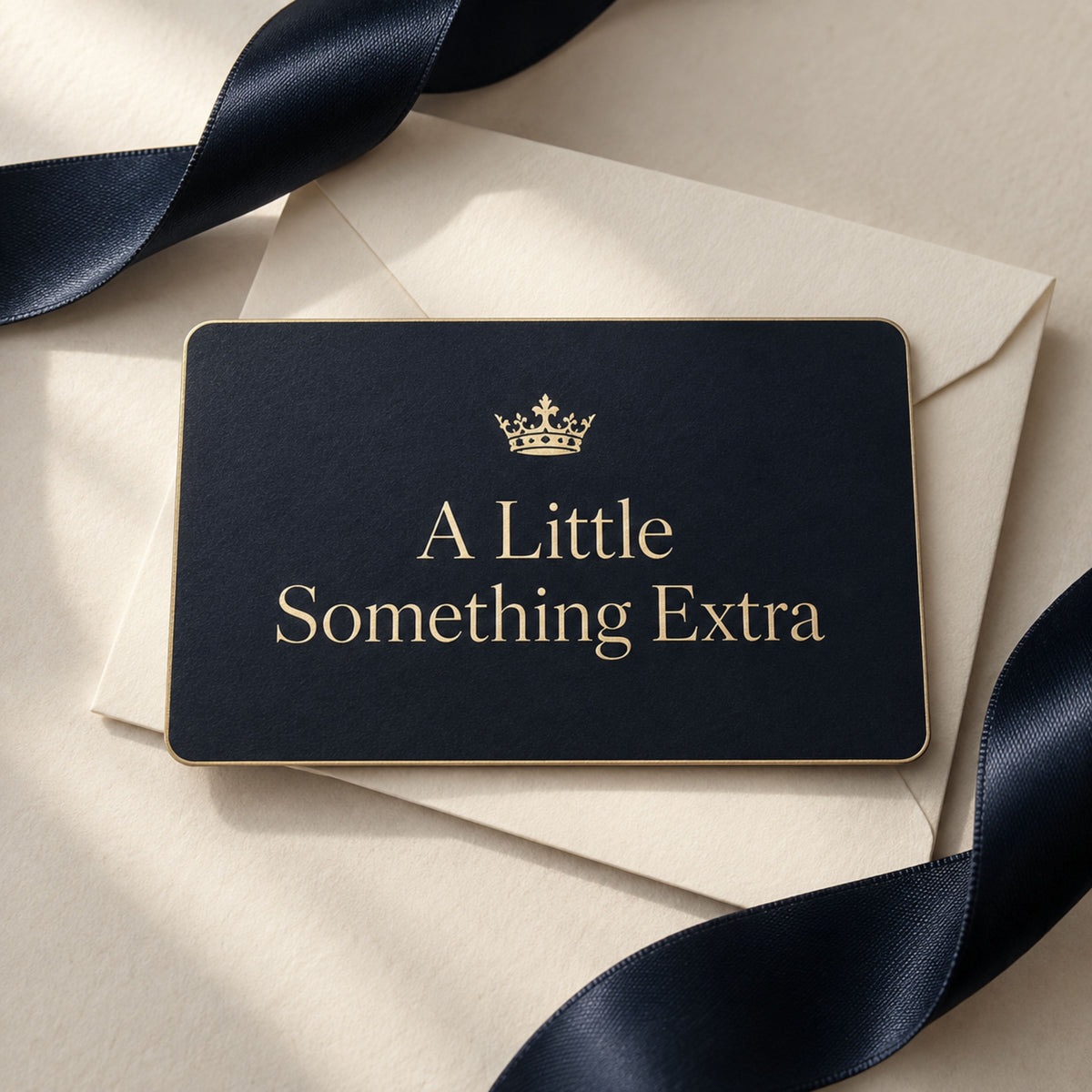 Midnight navy Zestful Productions digital gift card with a metallic gold crown and the words A Little Something Extra. The card rests on an ivory envelope surrounded by navy satin ribbon in an elegant, neutral gift setting.