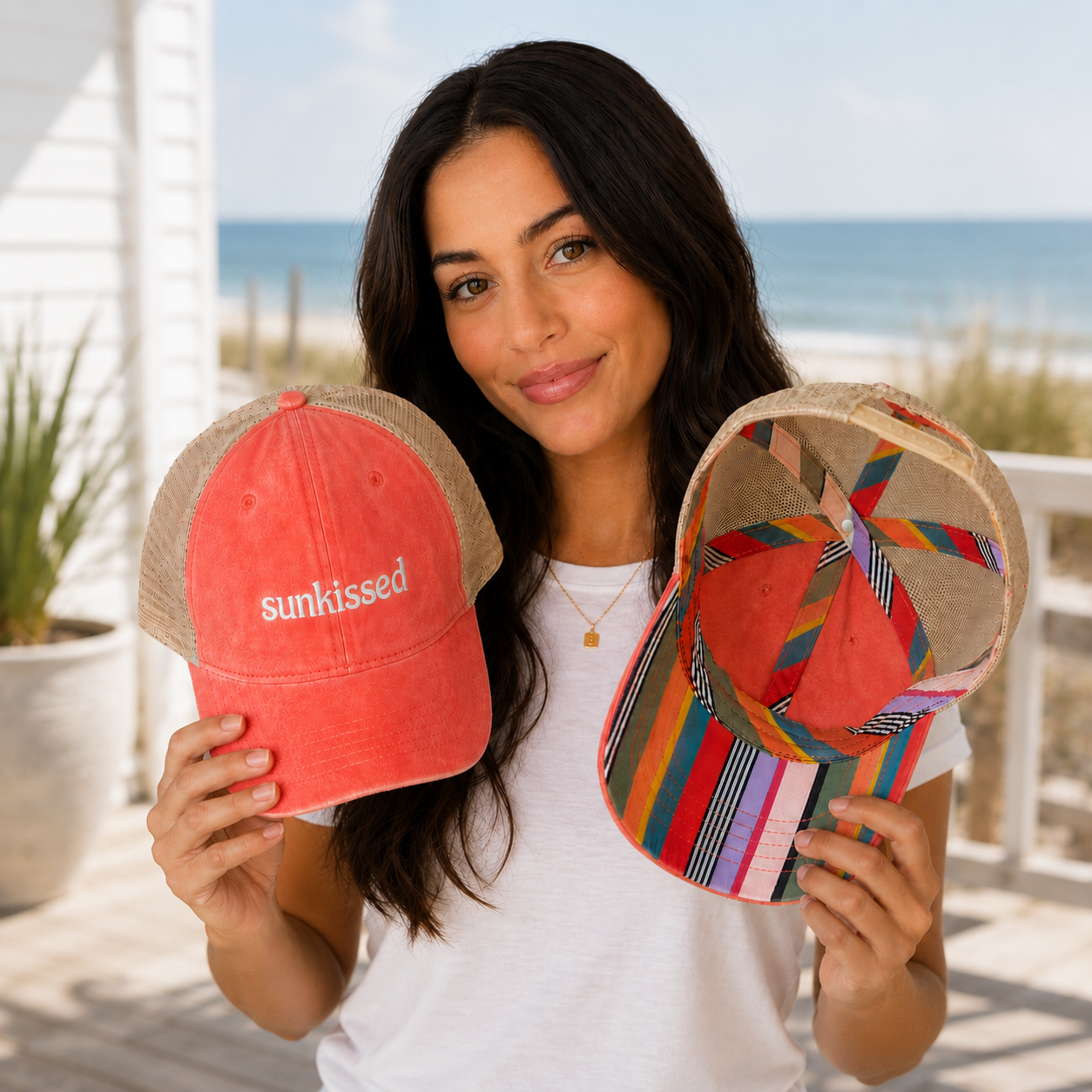 Woman holding coral sunkissed trucker hat with colorful striped underbrim in a coastal beach house setting for Zestful Productions hat collection
