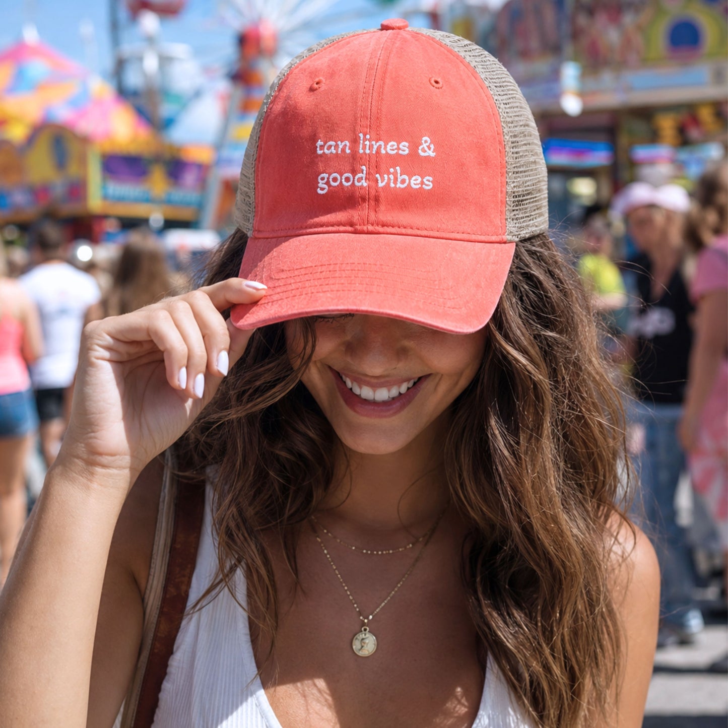 Woman wearing tan lines and good vibes coral trucker hat at a colorful summer carnival fair