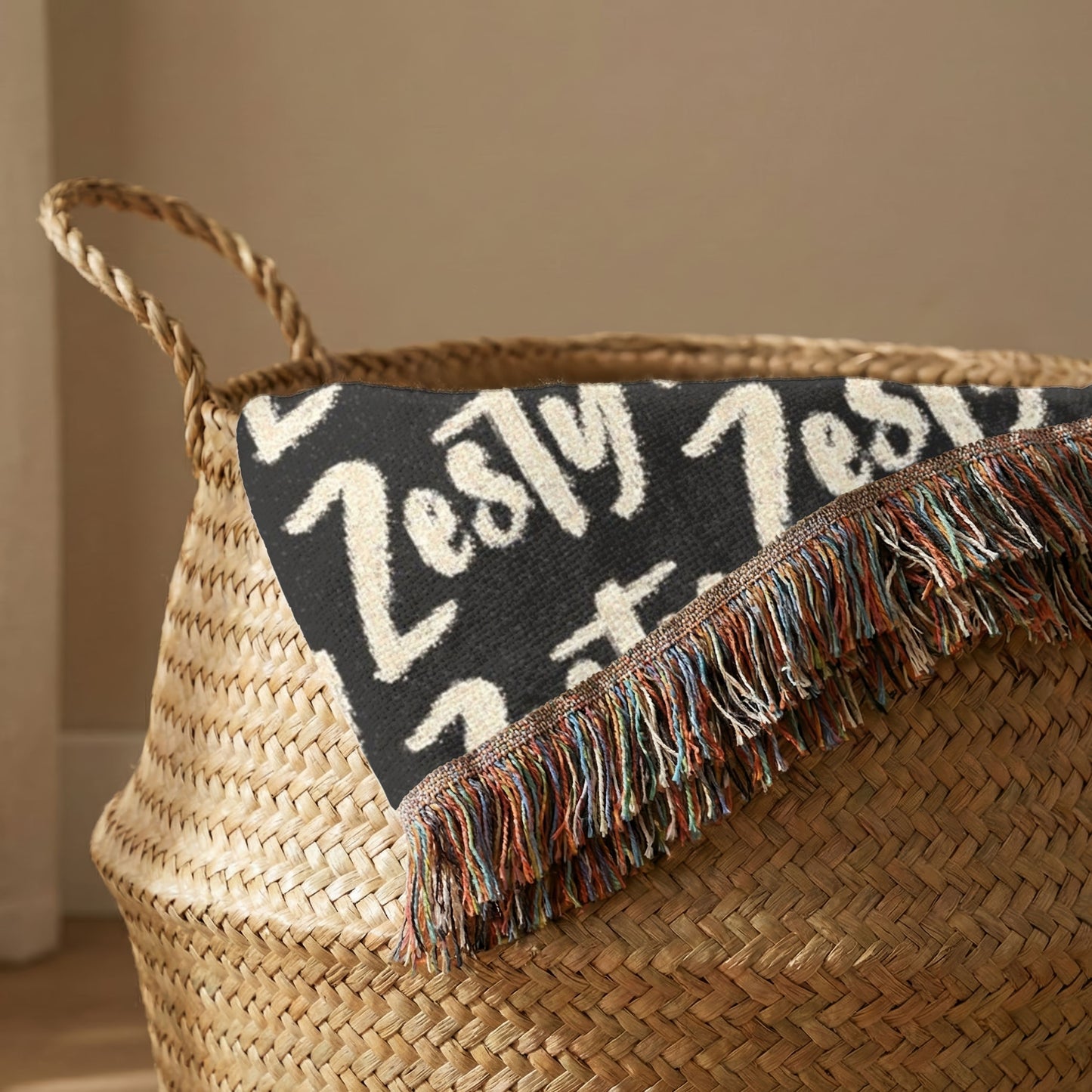 Woven basket with a black blanket featuring white text and colorful fringe.